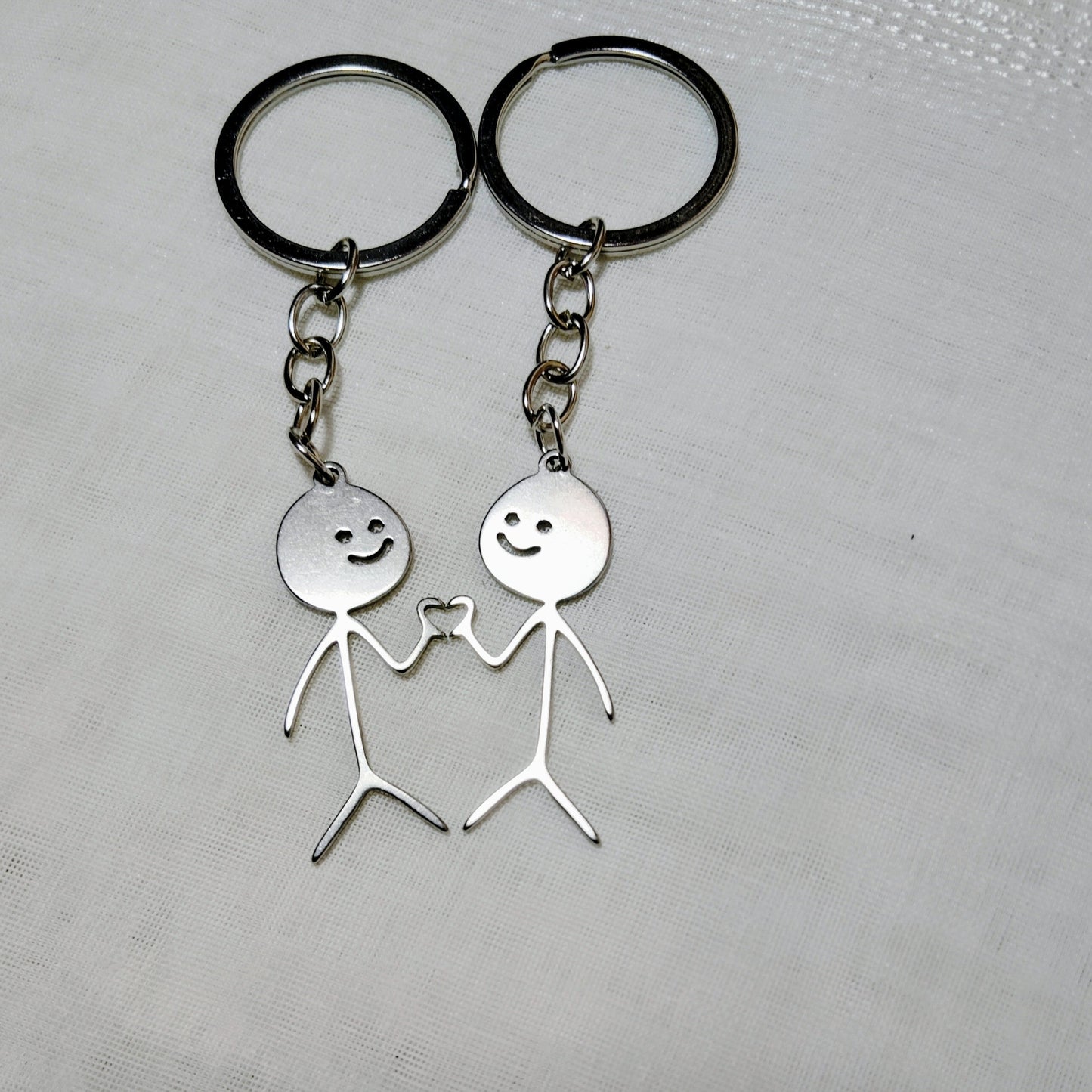 Two silver keychains with stick figure designs on a textured surface