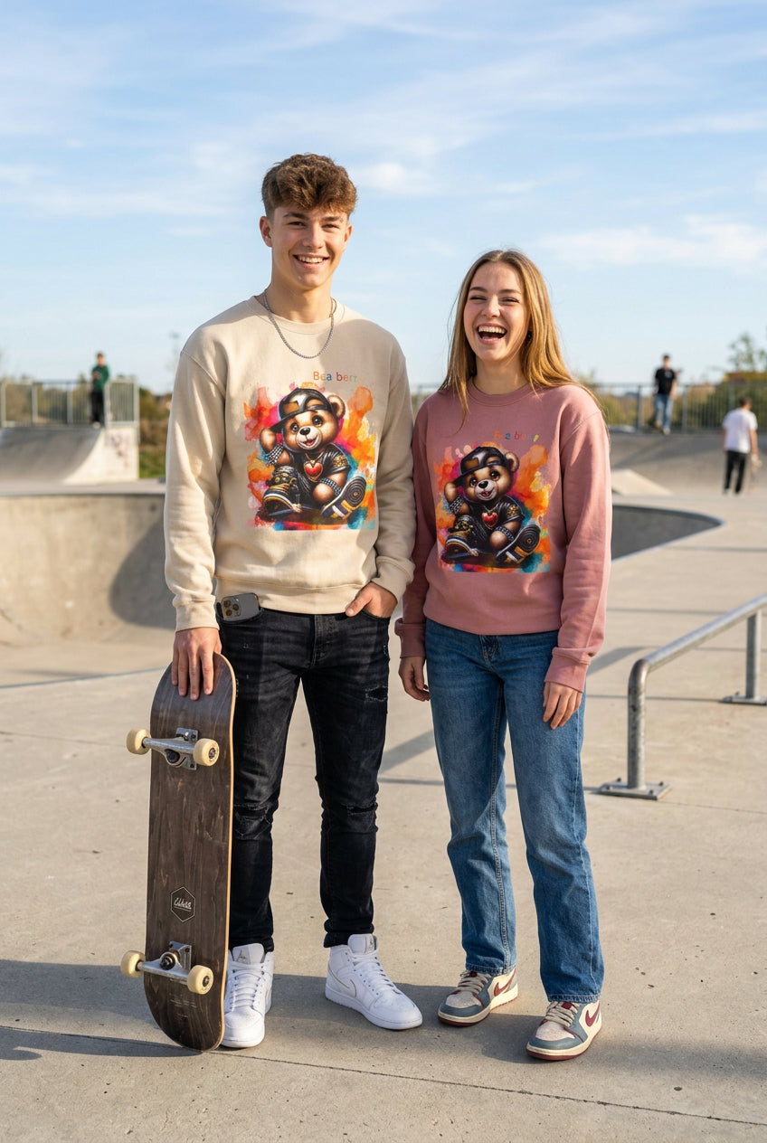 A beige crewneck sweatshirt featuring a colorful graphic of a cartoon bear wearing a black cap and outfit, sitting on a skateboard with the text 'Bea ber' above it, displayed on a clean white background.