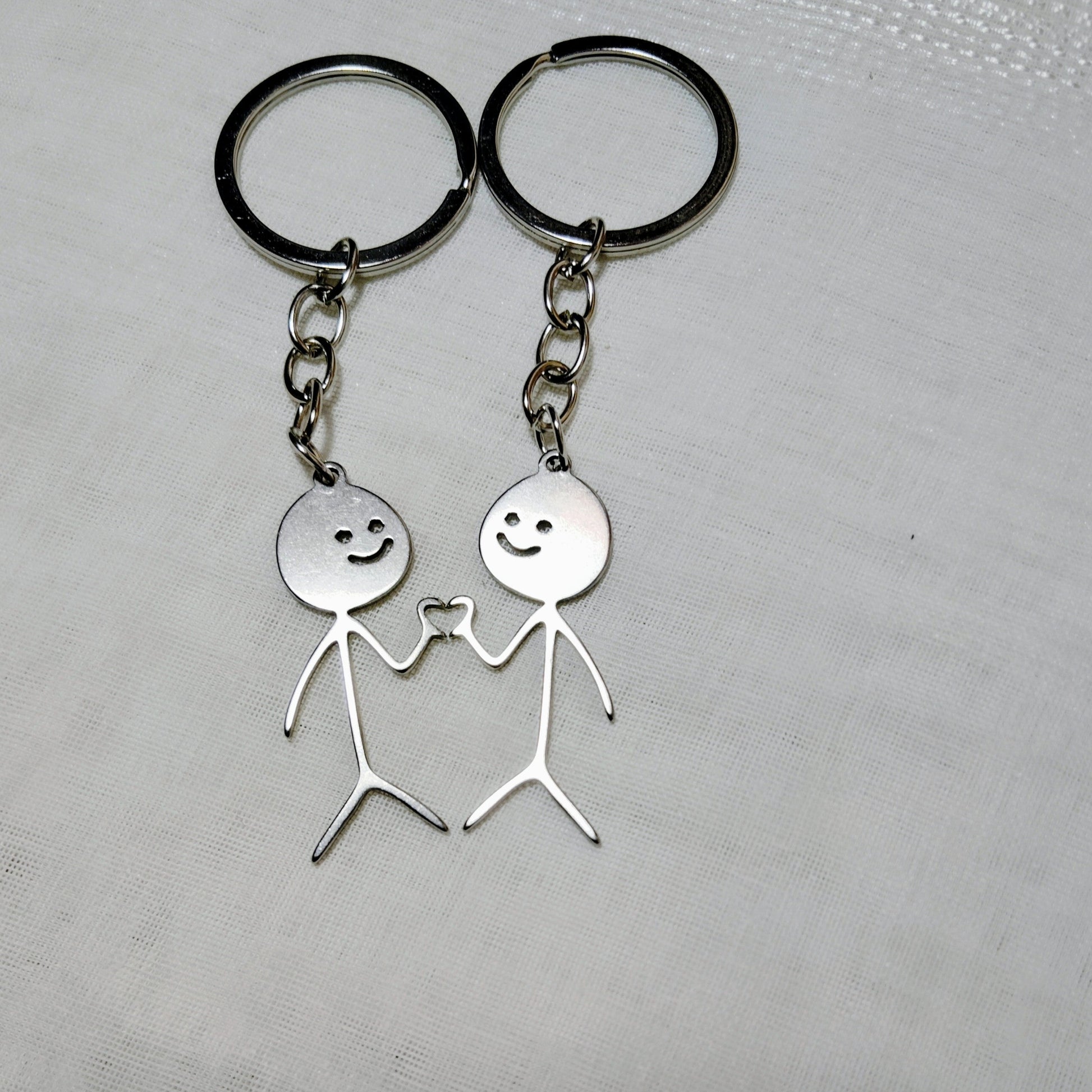 Two silver keychains with stick figure designs on a textured surface