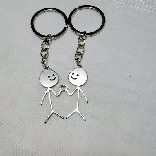 Two silver keychains with stick figure designs on a textured surface